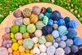 Many colorful balls, clews, wads, ravels of wool, laying in a large wooden bowl standing on the ground of green grass