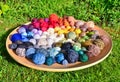 Many colorful balls, clews, wads, ravels of wool, laying in a large wooden bowl standing on the ground of green grass