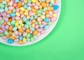Many colorful candy jelly beans on porcelain plate laying on light green surface