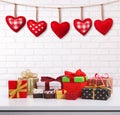 Many colorful gift boxes with ribbon bow on white table and white brick wall with vintage red heart shape garland. Valentines day Royalty Free Stock Photo