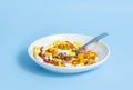 Many colorful pills, omega 3 vitamins and nutrition supplements in white plate with spoon on blue background. Medical