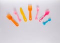 Many colorful plasic forks, spoons and knives on white background with copy space, top view. Devices for baby food Royalty Free Stock Photo