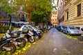 Many colorful scooters and cars parked on a street in central Rome