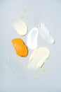 Many cosmetic products samples with vitamin C - cream and gel smears, oil drops over light gray background