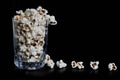 Many crunchy popcorns are in a clear glass on a dark black background, food or sneak for the movies and the circus. A dark high