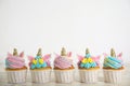 Many cute sweet unicorn cupcakes on white wooden table