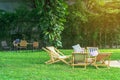 Many deck chairs and pillows with wooden table in the courtyard is surrounded by shady green grass. Comfortable pillows on outdoor