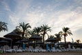 Many deck chairs on sandy beach in sunrise.