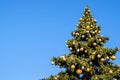 Many decorations and garland on a big faux Christmas tree outdoors on a blue sky background