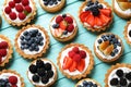 Many different berry tarts on blue wooden table, flat lay.