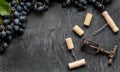 Many different corkscrews with open wine corks on dark concrete background in frame made of black grapes. Degustation winetasting