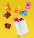 Many different gift boxes falling into paper shopping bag on yellow background Royalty Free Stock Photo