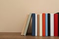Many different hardcover books on wooden table near beige wall. Space for text