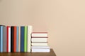 Many different hardcover books on wooden table near beige wall. Space for text