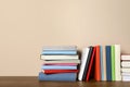 Many different hardcover books on wooden table near beige wall. Space for text