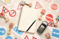 Many different road signs, notebook with sketch of roundabout and toy car on white wooden background, flat lay. Driving school