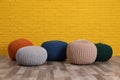 Many different stylish poufs on floor near yellow brick wall in room