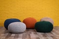 Many different stylish poufs on floor near yellow brick wall in room