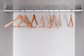 Many empty, lacquered light wood clothes hangers hang in wardrobe on metal rod. Internal space of furniture