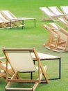 Many empty white deck chairs with tables in lawn is surrounded by shady green grass. Comfortable on outdoor patio chairs in garden Royalty Free Stock Photo