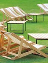 Many empty white deck chairs with tables in lawn is surrounded by shady green grass. Comfortable on outdoor patio chairs in garden Royalty Free Stock Photo