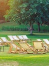 Many empty white deck chairs with tables in lawn is surrounded by shady green grass. Comfortable on outdoor patio chairs in garden Royalty Free Stock Photo