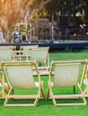 Many empty white deck chairs with tables in lawn is surrounded by shady green grass. Comfortable on outdoor patio chairs in garden Royalty Free Stock Photo