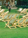 Many empty white deck chairs with tables in lawn is surrounded by shady green grass. Comfortable on outdoor patio chairs in garden Royalty Free Stock Photo