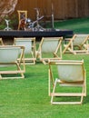 Many empty white deck chairs with tables in lawn is surrounded by shady green grass. Comfortable on outdoor patio chairs in garden Royalty Free Stock Photo