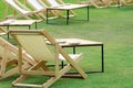 Many empty white deck chairs with tables in lawn is surrounded by shady green grass. Comfortable on outdoor patio chairs in garden Royalty Free Stock Photo