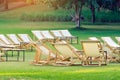 Many empty white deck chairs with tables in lawn is surrounded by shady green grass. Comfortable on outdoor patio chairs in garden Royalty Free Stock Photo