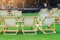 Many empty white deck chairs with tables in lawn is surrounded by shady green grass. Comfortable on outdoor patio chairs in garden Royalty Free Stock Photo