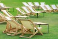 Many empty white deck chairs with tables in lawn is surrounded by shady green grass. Comfortable on outdoor patio chairs in garden Royalty Free Stock Photo