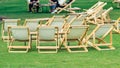 Many empty white deck chairs with tables in lawn is surrounded by shady green grass. Comfortable on outdoor patio chairs in garden Royalty Free Stock Photo