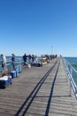 Many fisherman along the rail fence on one side of a long pier fishing in the ocean