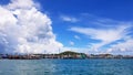 Many fishing boat parked on sea at port near coast and community with blue sky, white clouds and green mountain background Royalty Free Stock Photo