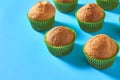 Many fluffy muffins in green paper molds scattered on blue background