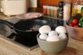 Many fresh eggs on wooden countertop in kitchen. Frying bacon for breakfast