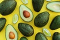 Many fresh whole and cut avocados with limes on yellow background, flat lay