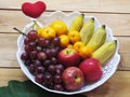 Many fruits that are beneficial to the body put together in a white tray with oranges, bananas, grapes and apples on wooden