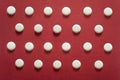 Many generic small round white pills, lots of little tablets on red background close up. Simple group of little pills, medicine