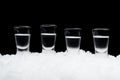 Many glasses of vodka standing on ice on black background Royalty Free Stock Photo