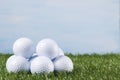 Many golf balls lie on the green grass agains the blue sky