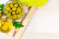 Many green whole olives and olive oil in the glass bowls on light wooden board background in the kitchen top view with copy space. Royalty Free Stock Photo