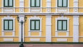 Green wooden windows on vintage yellow and white building wall with street lamp post on empty stone tile pavement Royalty Free Stock Photo