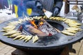 Many grilled smelt on a large round flat grill with open fire hole in the center, seafood cooking Royalty Free Stock Photo