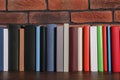 Many hardcover books on wooden table near brick wall