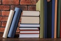 Many hardcover books on wooden table near brick wall