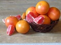 Many juicy orange shiny ripe grapefruit and some pieces of pilled skinned fruit in a basket on oak tree background.