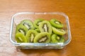 Many kiwi slices in a glass crisper on a wooden table. Kiwifruit slices without peel